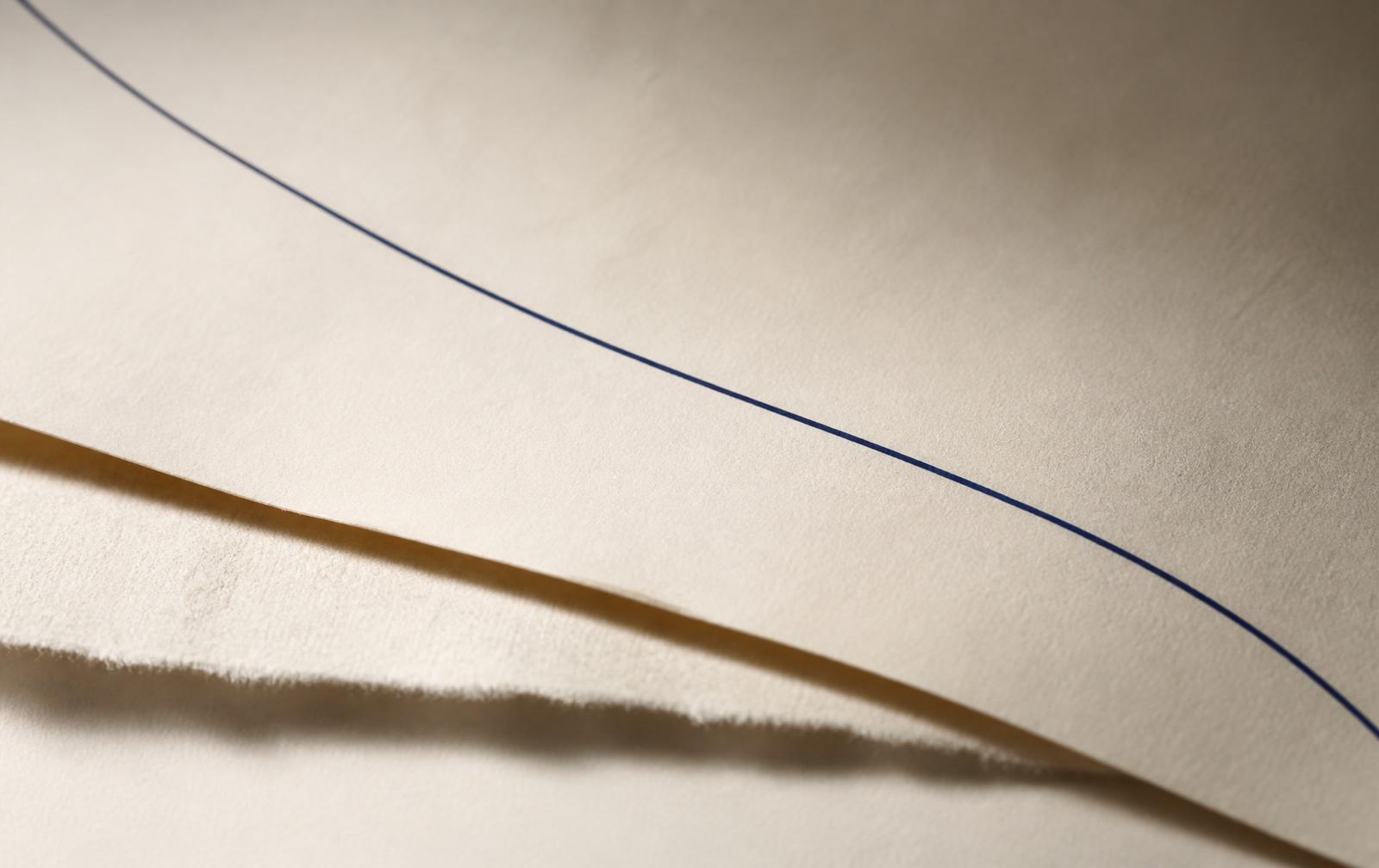 Layered ivory paper with a single fine navy line, in raking light